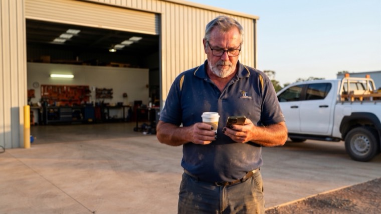 A trades business owner on site in the morning with a coffee and his phone